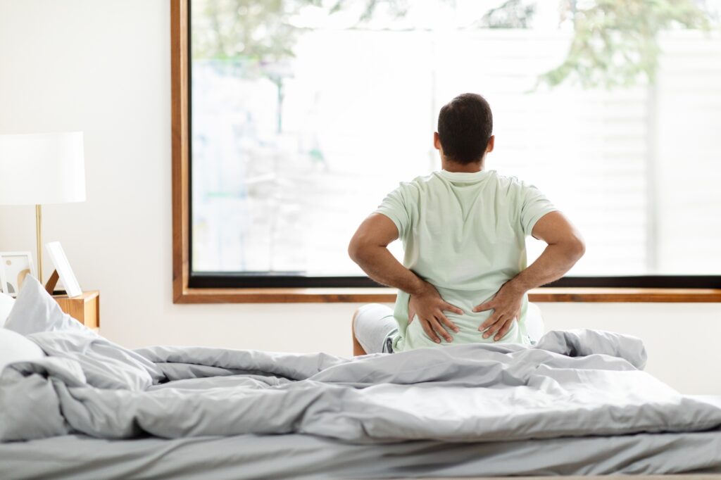 Tired black man suffering from back pain after waking up